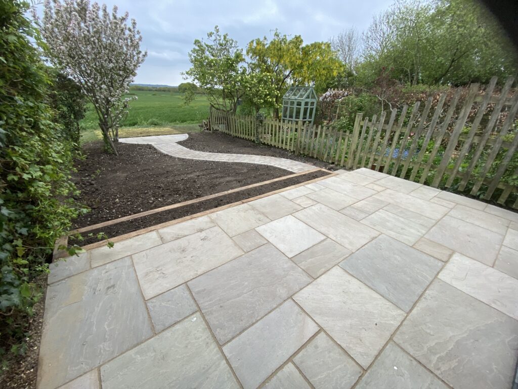 Indian sandstone patio beside a garden and lawn