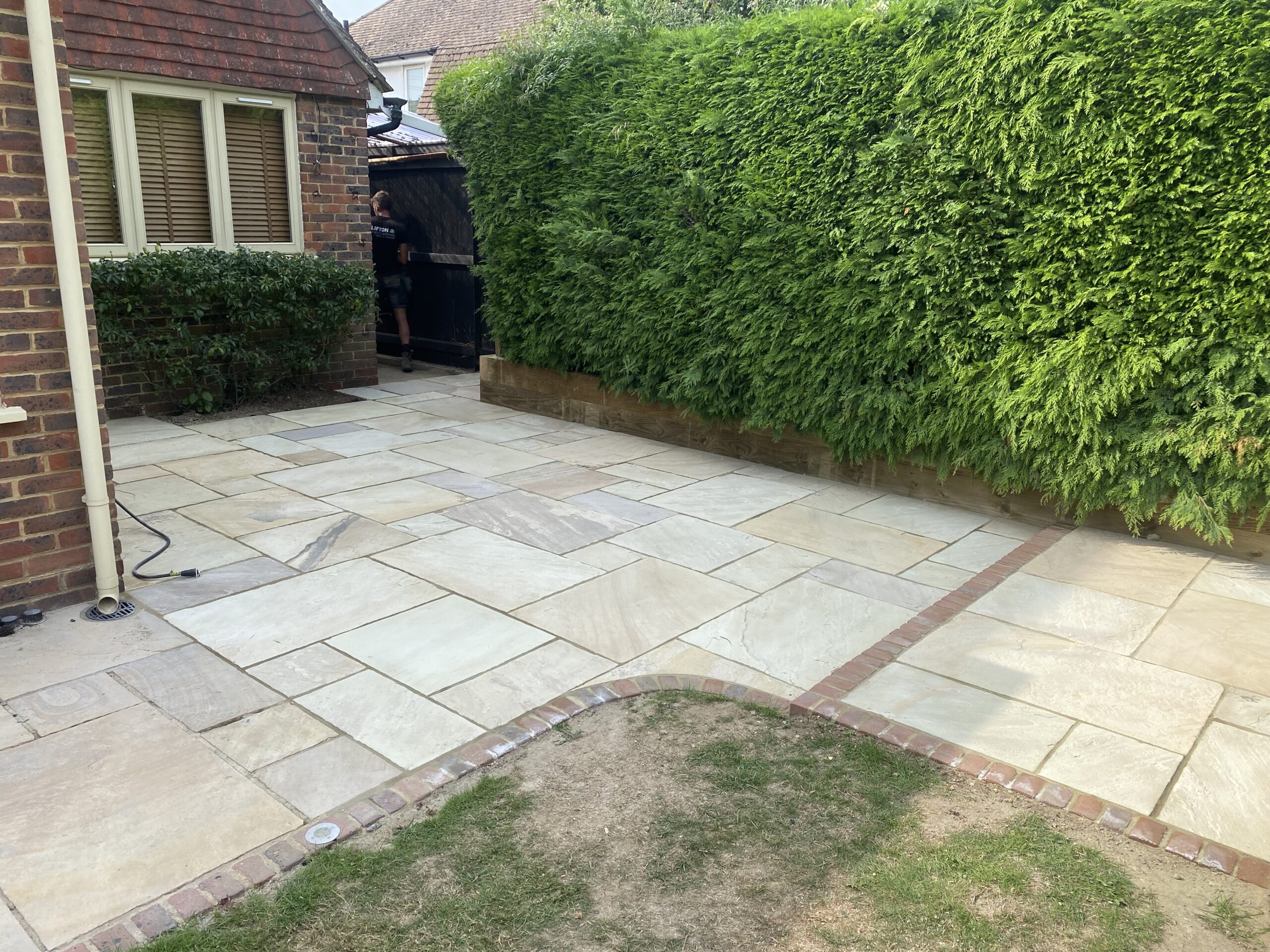 Indian sandstone patio with brick edging beside a lawn